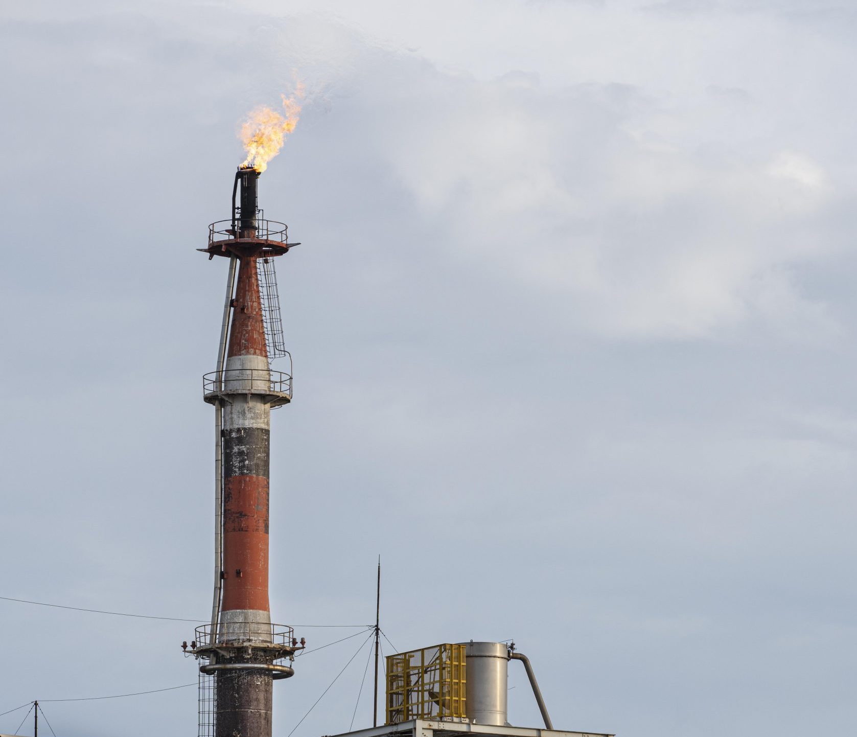 Industrial flare stack burning against a grey sky, the kind of emission source monitored in climate research.