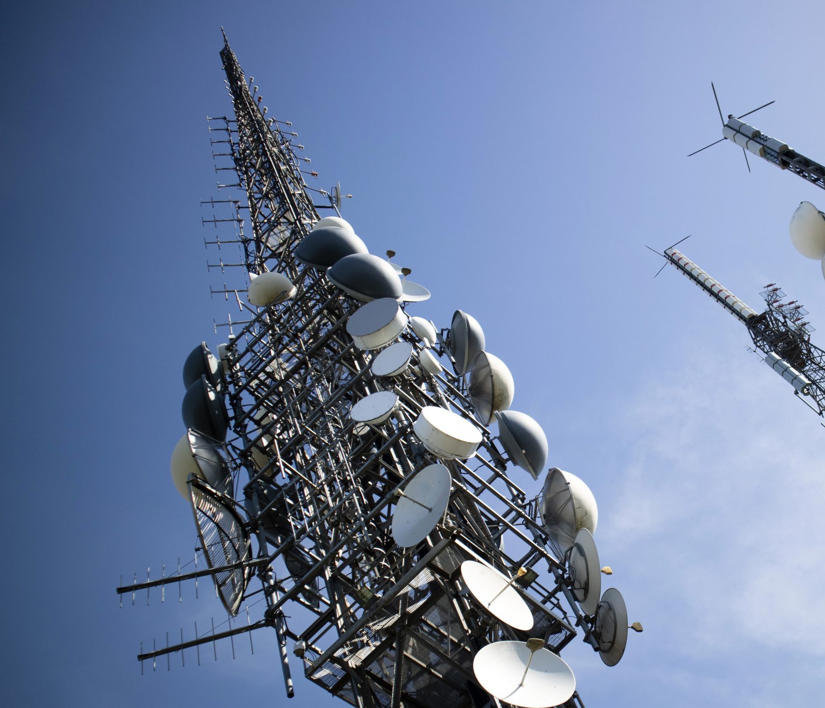 Telecommunications mast seen from below, carrying rows of parabolic antennas against a blue sky.